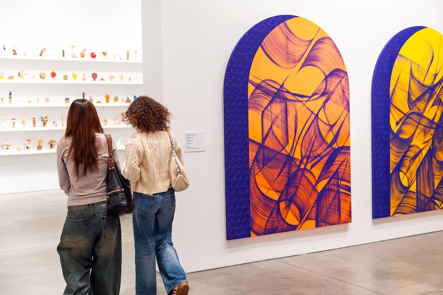 Two people with long hair walk past large, colorful abstract paintings with swirling purple and orange patterns at ICA Boston. Small sculptural pieces are displayed on shelves in the background during Martin Luther King Day.