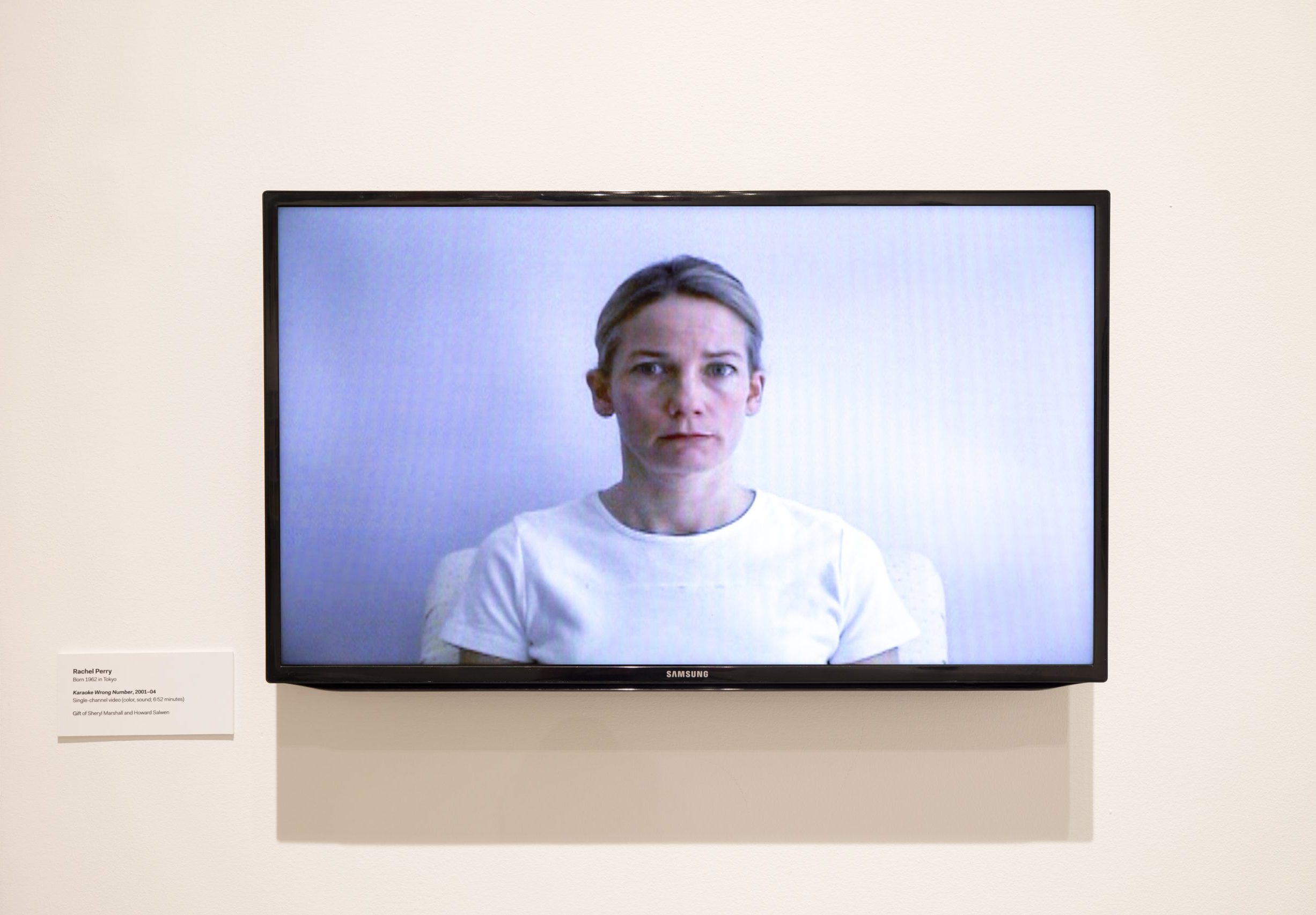A TV screen displaying a woman in a white shirt against a white background