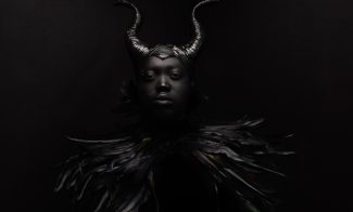 Dark photo of figure wearing horns and feathers