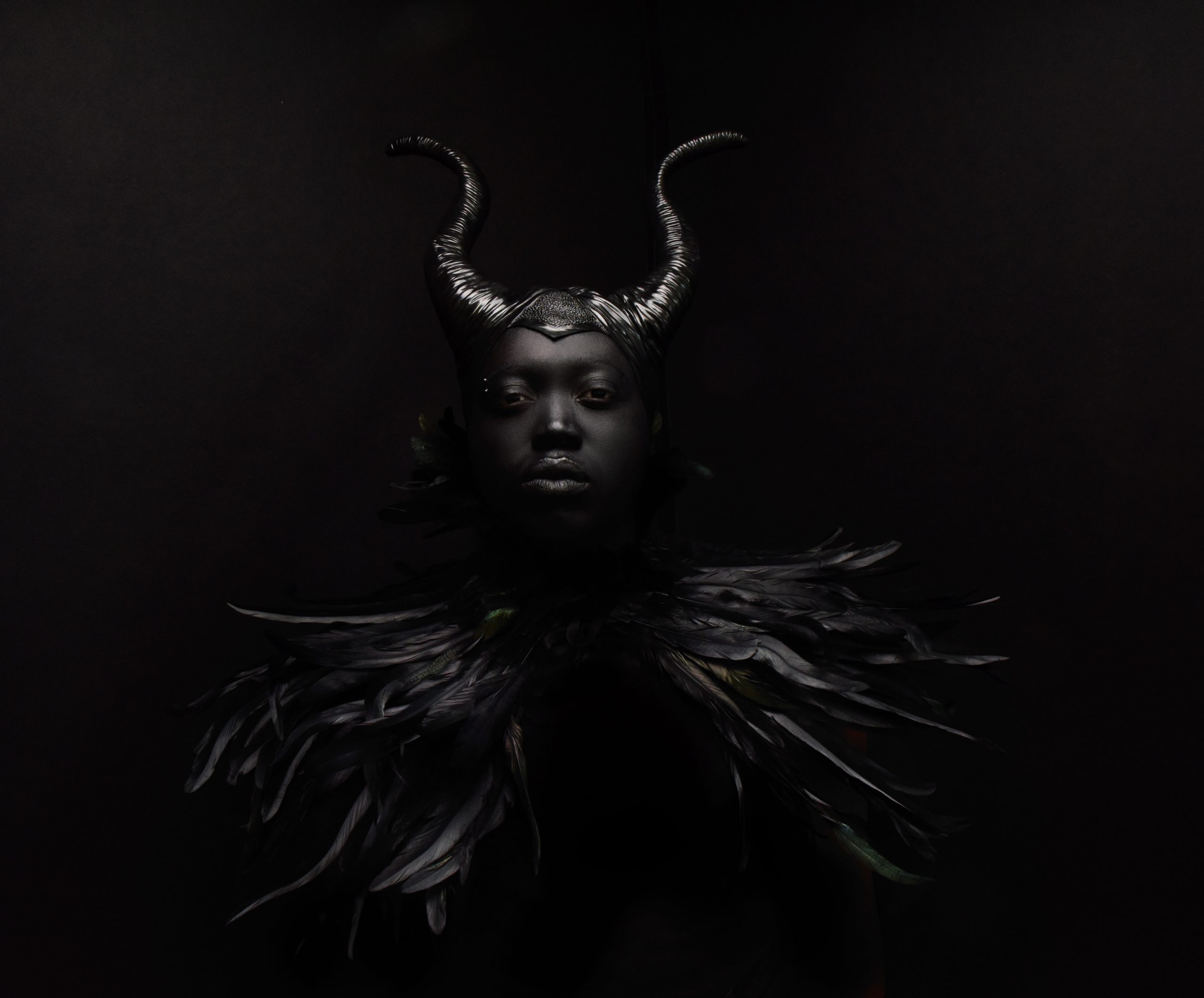 Dark photo of figure wearing horns and feathers