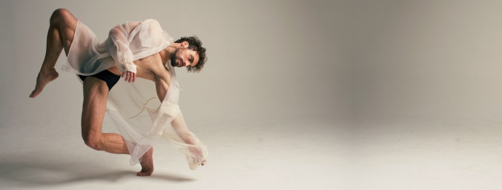 Man in see-through robe in a dance pose on one foot