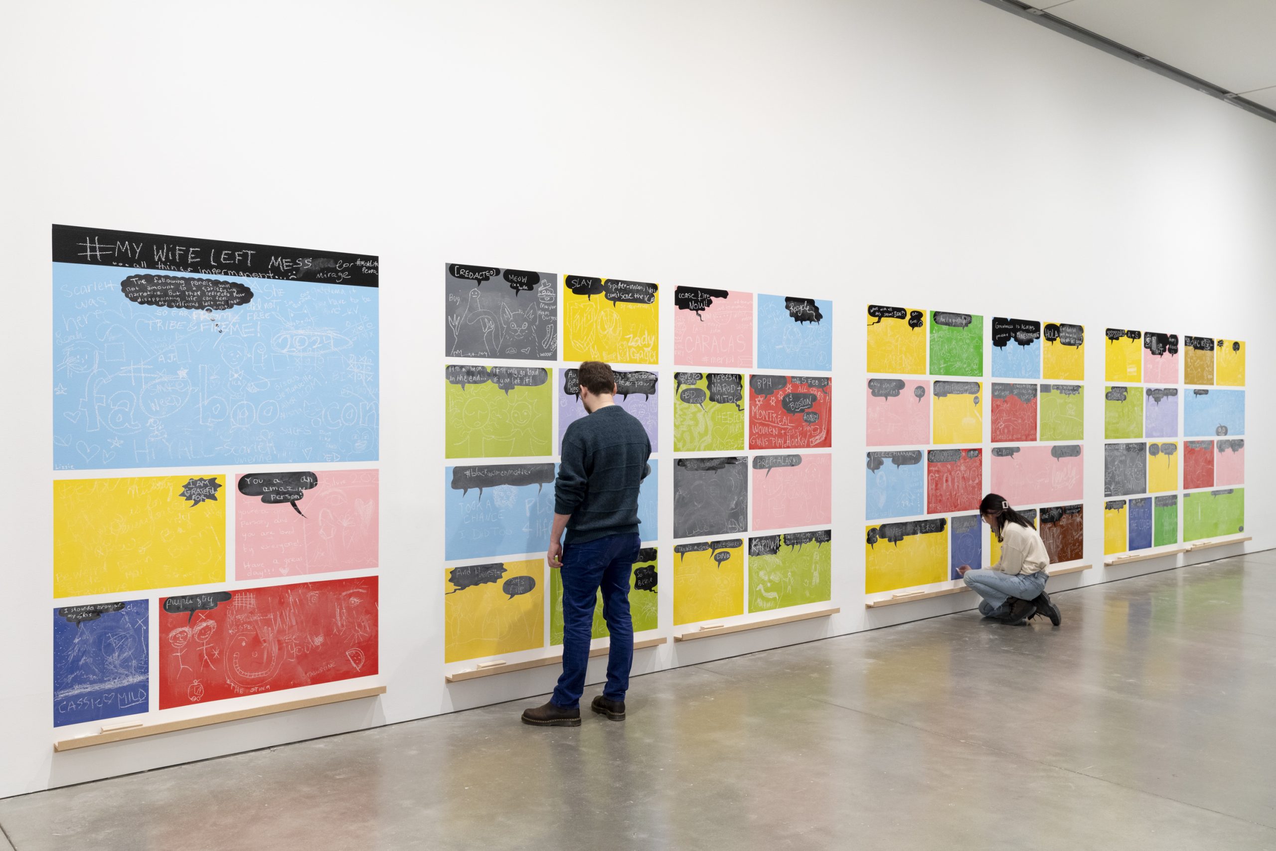 Two people drawing on a wall installation of colorful chalkboard tiles covered in chalk writing and drawing