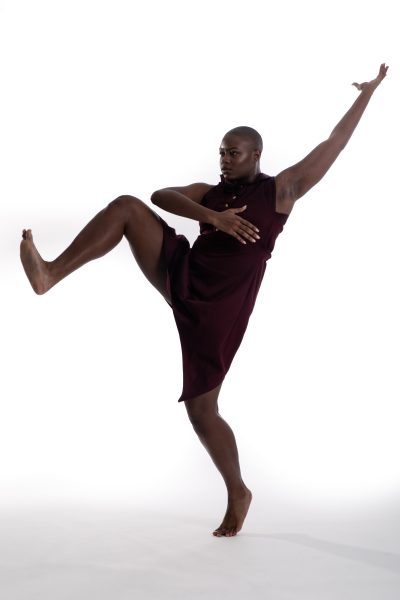 a dancer in a black tank and black shorts lifts one leg in the air and one arm in the air