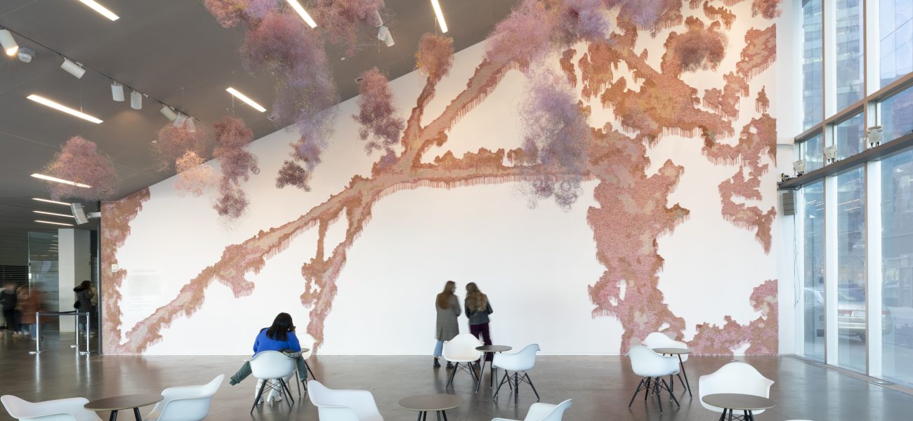 Pink fringed material installed on a slanted lobby wall with hanging pink forms