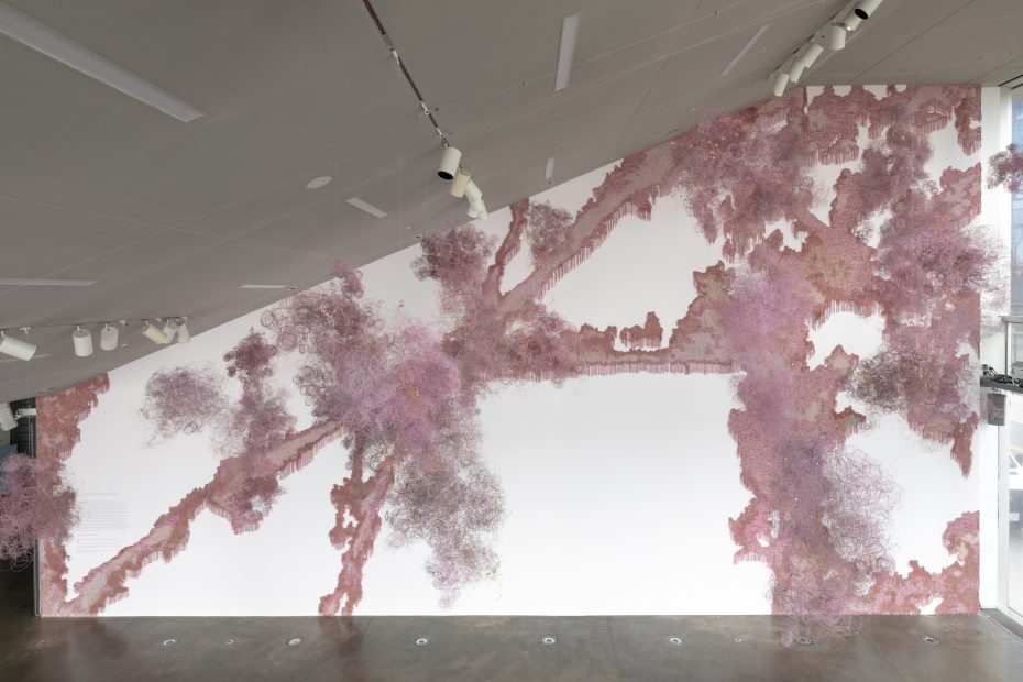 Pink fringed material installed on a slanted lobby wall with hanging pink forms