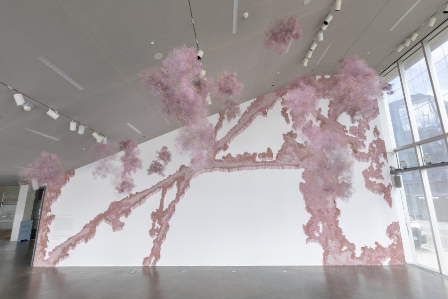 Pink fringed material installed on a slanted lobby wall with hanging pink forms