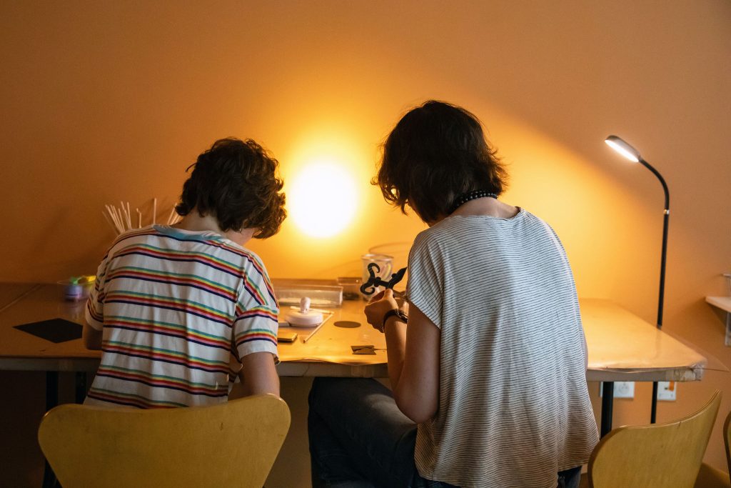 Two people with curly hair cutting an animal out of black paper