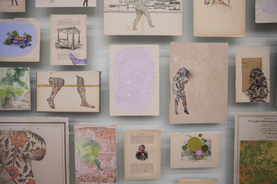 A salon-style installation of drawings, many on repurposed book pages, of colorful patterned female figures, body parts, and dots.