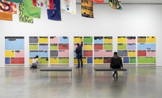 Visitors writing or drawing on a wall installation comprised of colorful tiles in a gallery