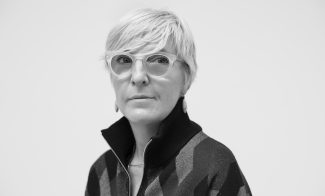 black and white photo of helen molesworth. a woman with short blonde hair and big ciruclar glasses in a quarter zip
