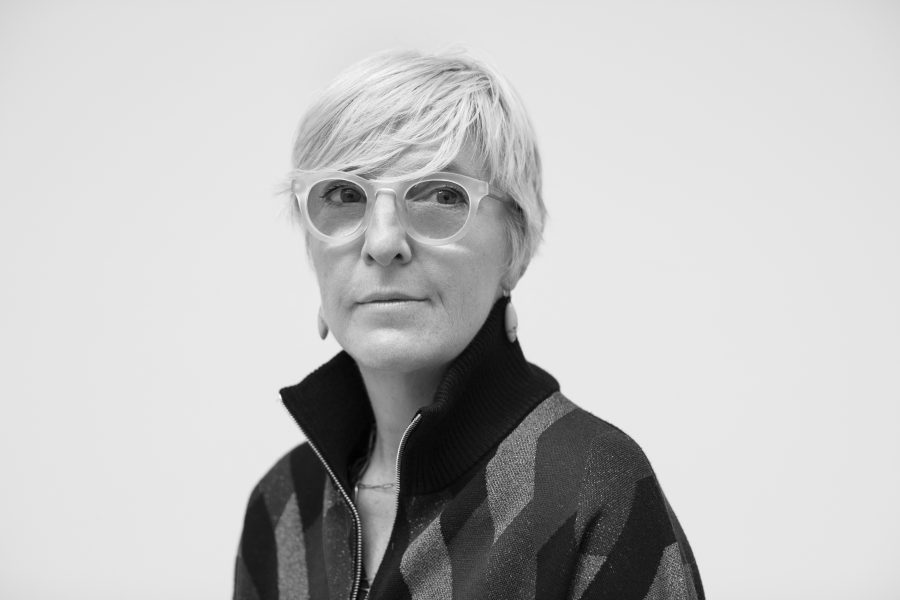 black and white photo of helen molesworth. a woman with short blonde hair and big ciruclar glasses in a quarter zip