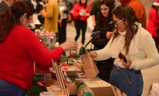 Shoppers in winter clothes in front of a table at an indoor market