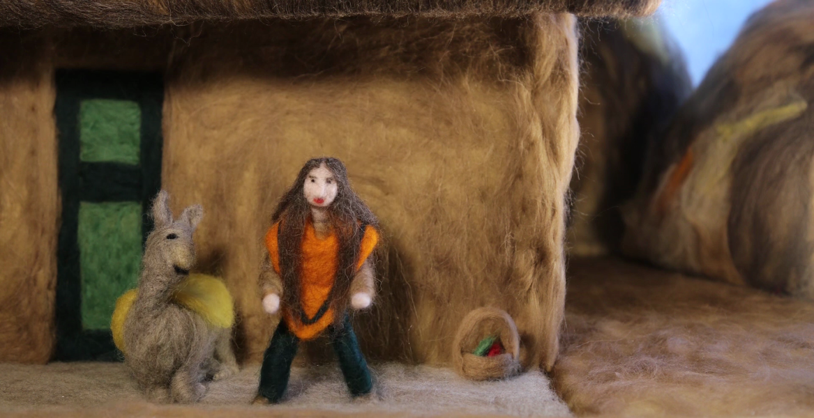 Needle felted scene with a doll in an orange poncho next to a llama