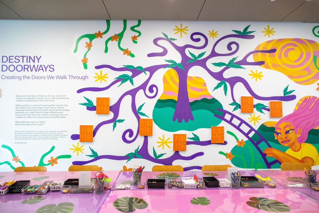 Wall with bright graphic of girl and tree with table full of art supplies in front of it