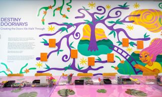 Wall with bright graphic of girl and tree with table full of art supplies in front of it