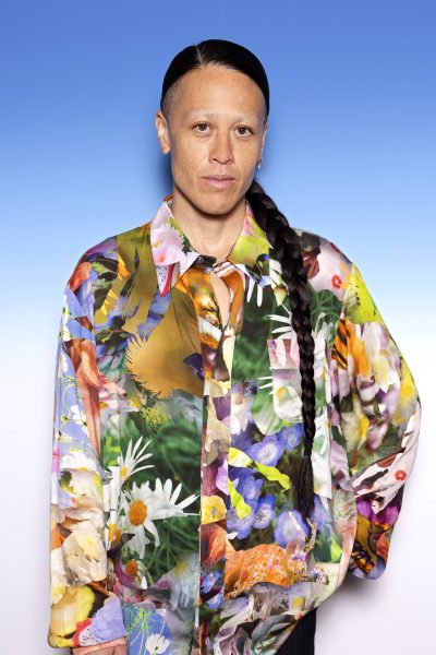Photo of a person with a long dark braid and colorful shirt against a blue background