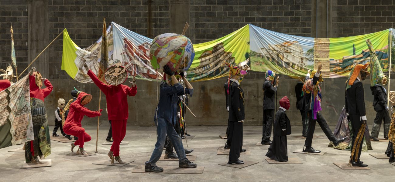 A line of figurative sculptures carrying a long banner