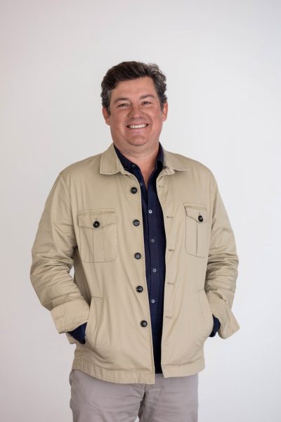 Person with short brown hair and tan jacket smiling