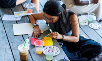 A person paints on paper with watercolors at an outdoor watercolor workshop.