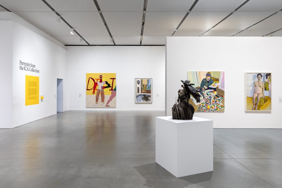 A gallery with white walls displaying colorful paintings and a dark bust on a pedestal in the center