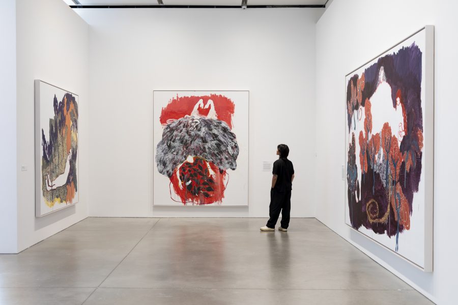 A person stands in a white-walled gallery, admiring large paintings with expressive brushstrokes and vibrant colors