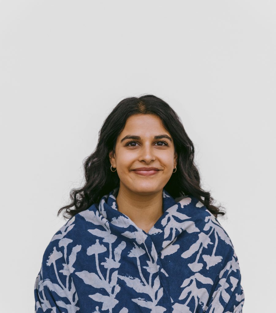 A person with long, dark hair smiles at the camera. They are wearing a blue and white floral patterned shawl.