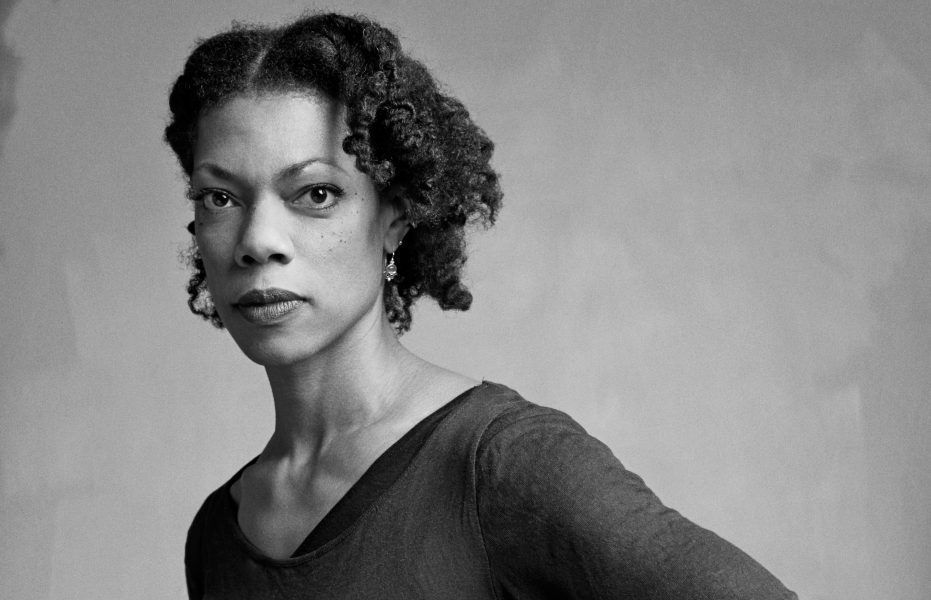 Black-and-white portrait of a woman with natural curly hair, wearing a dark top and small earrings, looking directly at the camera—an expressive image reminiscent of performers at Summer Stages Dance at ICA.