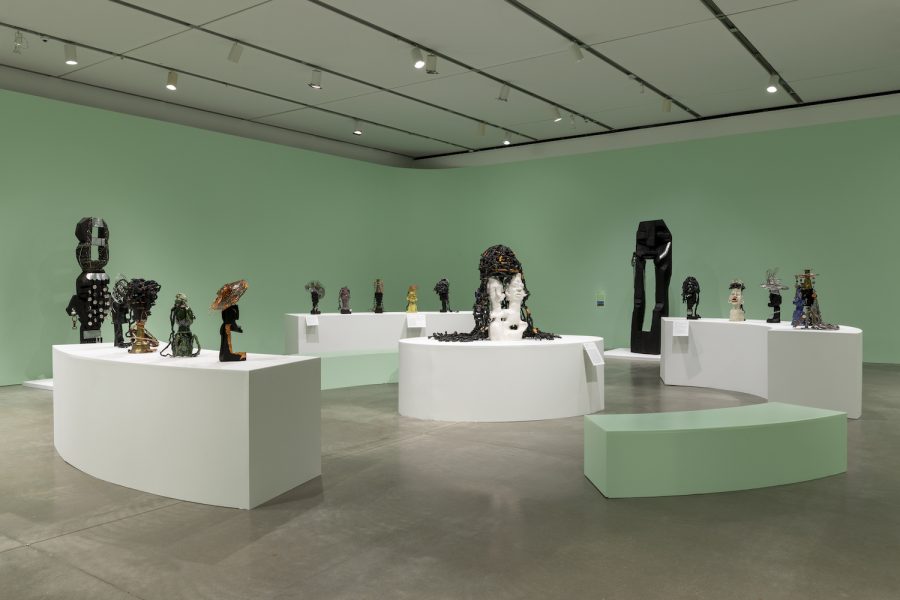 Sculptural artworks by Leilah Babirye are displayed on white plinths in a spacious gallery at ICA Boston, with mint-green walls and ceiling lights; a mint-green curved bench sits in the foreground.