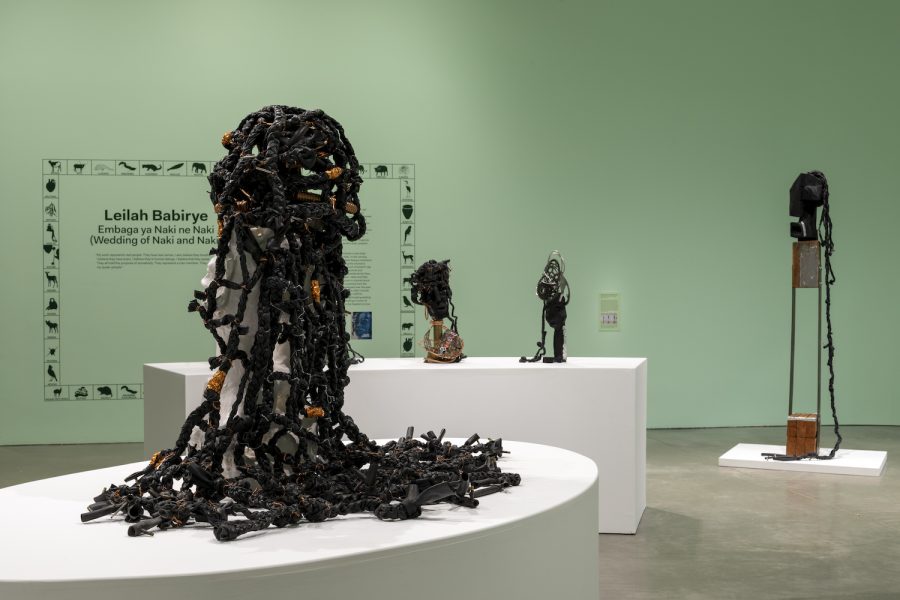 Sculptures made of dark, twisted materials with orange accents are displayed on white platforms in a green-walled gallery. Text on the wall introduces an exhibit by Leilah Babirye at ICA Boston.