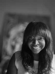 A woman with long dark hair and bangs smiles at the camera in a black and white portrait, taken during Artmaking After Dark at ICA Boston. She is wearing a light-colored top, and the background is softly blurred.