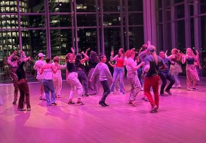 A group of people dance in a purple-lit indoor space at night.