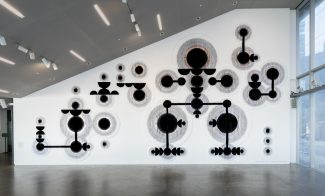 A large textured wall installation with abstract black circular and linear shapes arranged in a geometric pattern