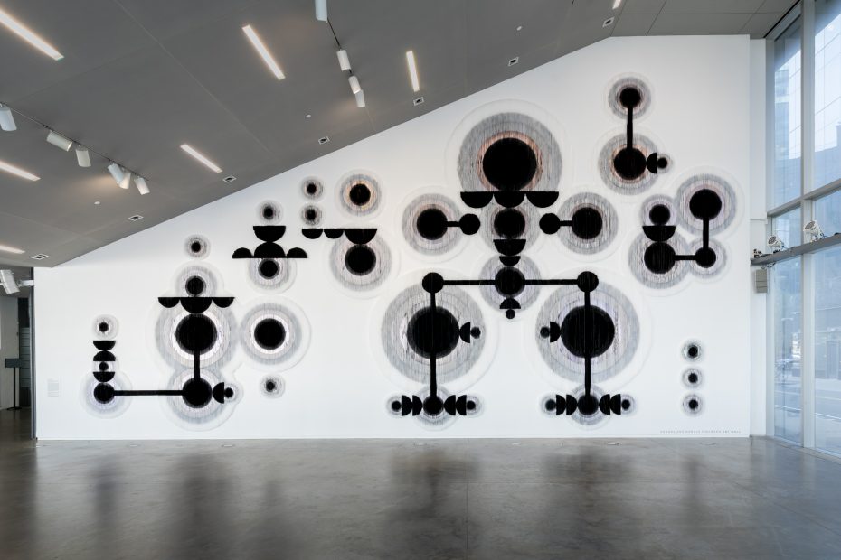 A large textured wall installation with abstract black circular and linear shapes arranged in a geometric pattern