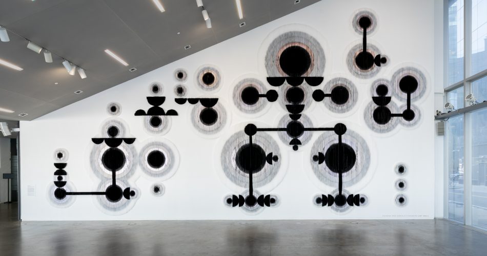 A large textured wall installation with abstract black circular and linear shapes arranged in a geometric pattern