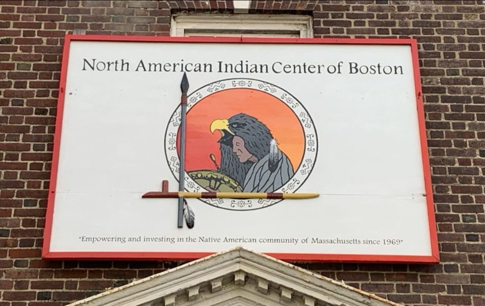 A sign reading North American Indian Center of Boston features a Native American person and eagle, with a spear and feather. Below, it says, Empowering and investing in the Native American community of Massachusetts since 1969.