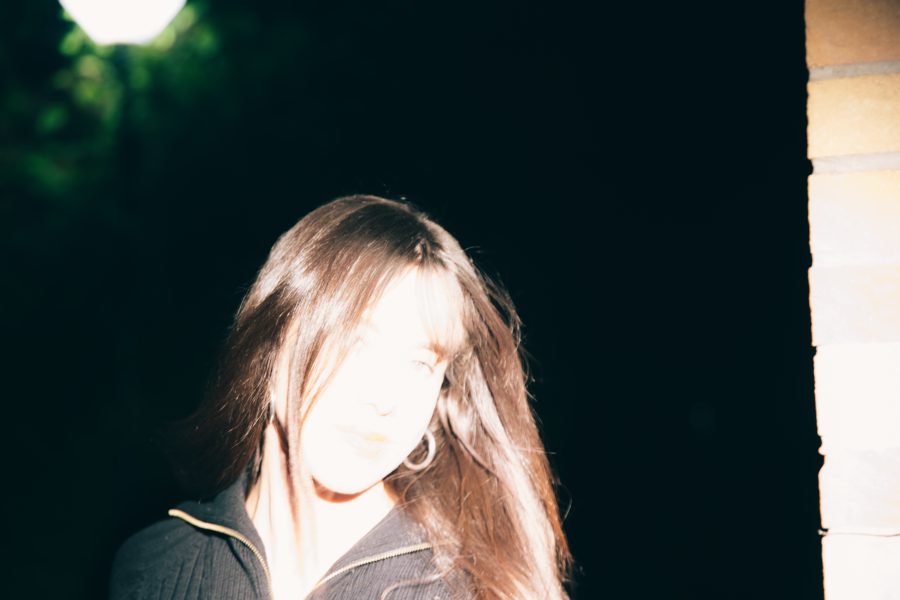 A person with long brown hair stands in partial darkness.