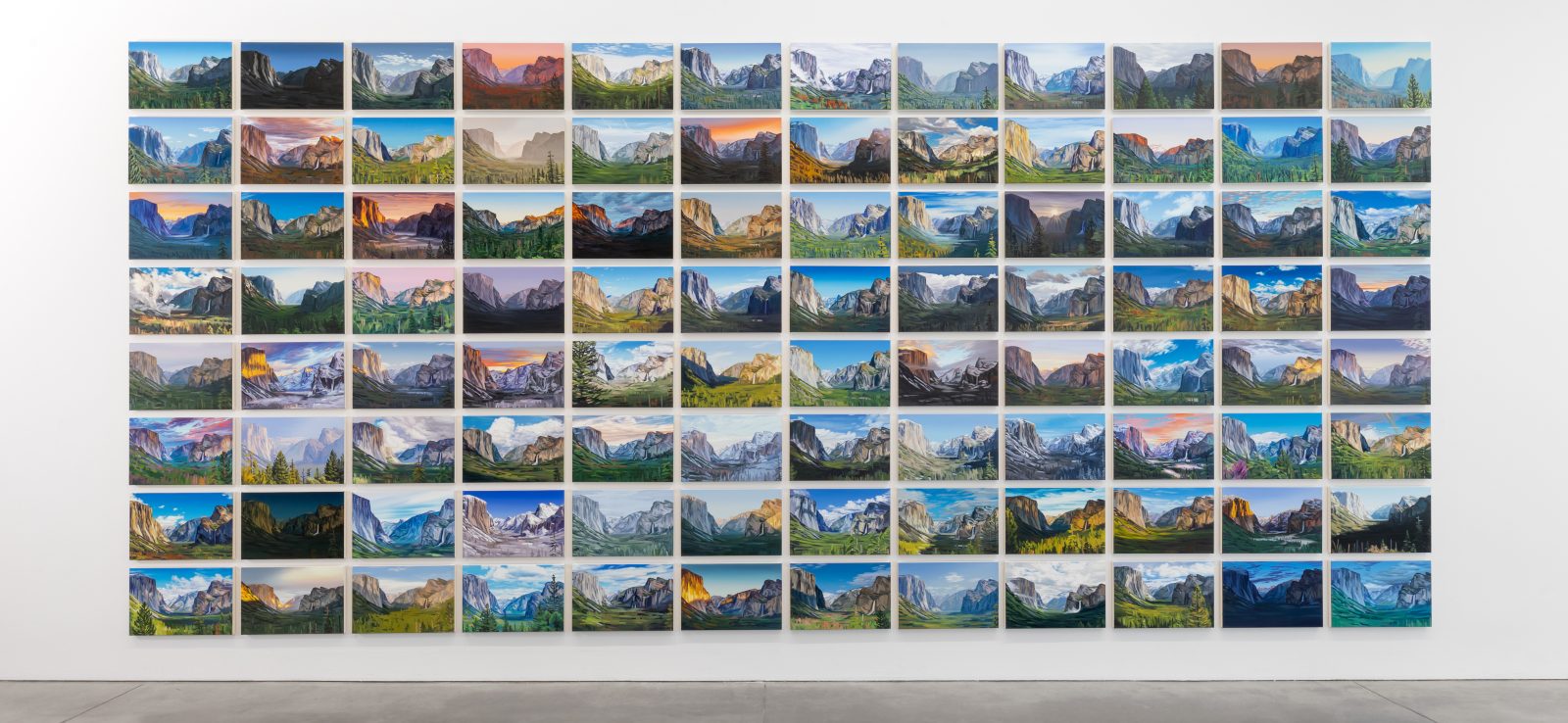 A gallery wall displays a grid of landscape photos, each showing different views and lighting of mountains, all neatly aligned in rows and columns above a polished concrete floor.