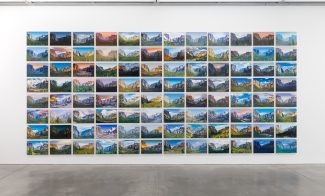A gallery wall displays a grid of landscape photos, each showing different views and lighting of mountains, all neatly aligned in rows and columns above a polished concrete floor.