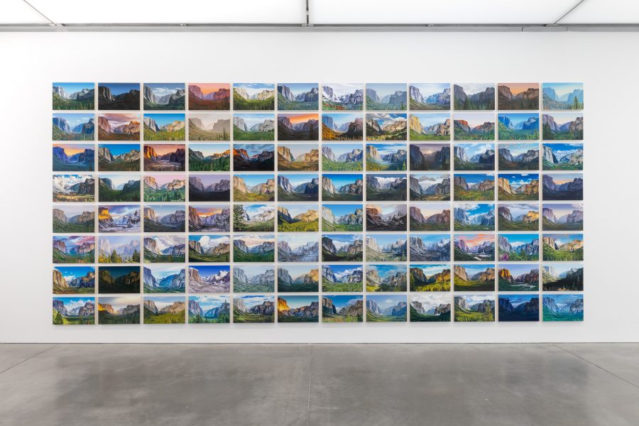 A gallery wall displays a grid of landscape photos, each showing different views and lighting of mountains, all neatly aligned in rows and columns above a polished concrete floor.
