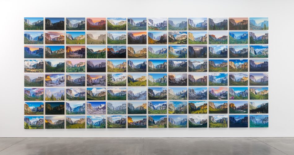 A gallery wall displays a grid of landscape photos, each showing different views and lighting of mountains, all neatly aligned in rows and columns above a polished concrete floor.