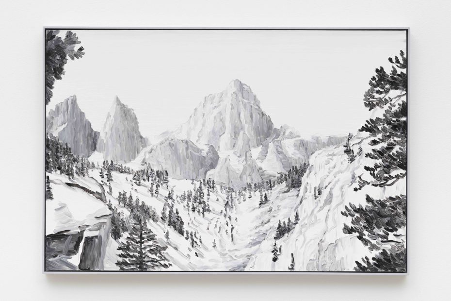 A black-and-white painting of a snowy mountain landscape with pine trees on the slopes and rocky peaks in the background, framed and hanging on a white wall.