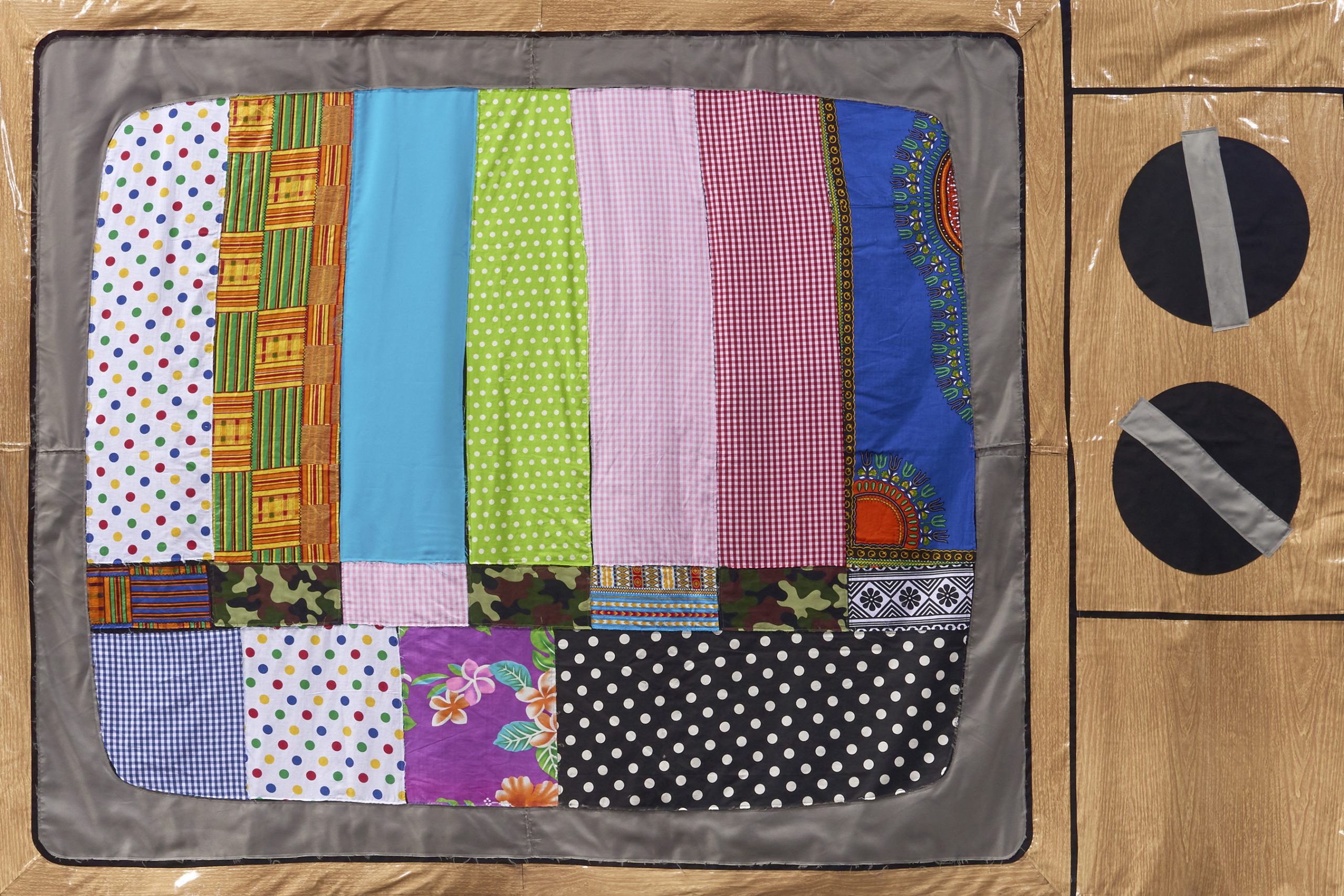 A handmade quilt designed to look like an old-fashioned TV displaying a colorful test pattern, reminiscent of an Opening Reception: Derrick Adams: View Master, with patchwork bars on the screen and two large black dials on the right side.