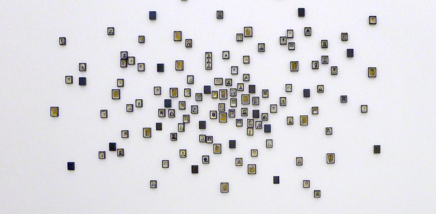 A white wall displays clusters of small, square tiles arranged in a loose, organic pattern, each tile containing simple black and white illustrations or symbols, with some yellow accents.