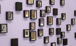 A lavender wall displays an arrangement of small, black-framed portraits in black and white—each featuring individual people