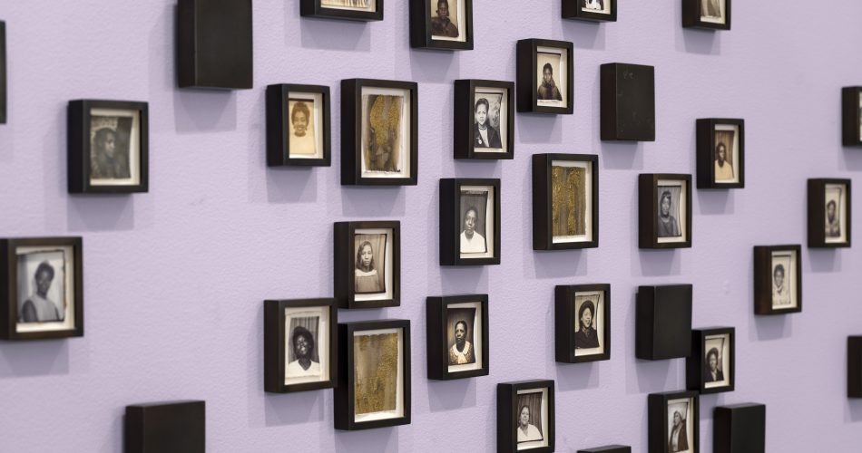 A lavender wall displays an arrangement of small, black-framed portraits in black and white—each featuring individual people