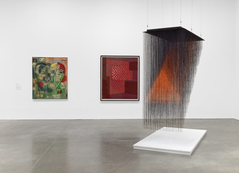 A gallery with two abstract paintings on a white wall and a large installation titled made of black and orange strings, suspended above a white platform. The space features a polished concrete floor.