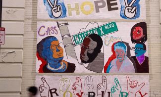 A mural on a brick wall features portraits of prominent Black figures, street signs reading Malcolm X Blvd, the word HOPE, peace signs, and ROXBURY spelled out in both letters and American Sign Language.