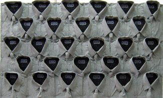 A wall display of 25 neatly arranged gray dress shirts, each buttoned up with the collars open and black fabric inside, giving the illusion of shirt fronts mounted on the wall. A light fixture is visible above.