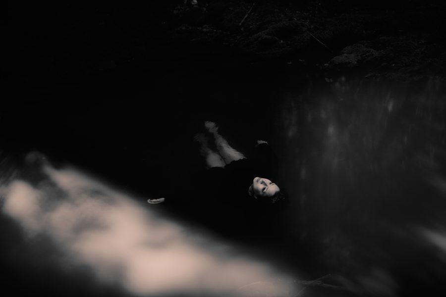 A person in dark clothing floats on their back in still water, with soft light and reflections illuminating part of the scene, creating a moody, mysterious atmosphere—evocative of the haunting soundscapes found in Colin Stetson and Brìghde Chaimbeul’s performances at ICA Boston.