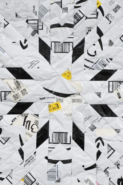 A geometric pattern made from overlapping white plastic shipping envelopes featuring black barcodes, Amazon logos, and yellow stickers, arranged to form a symmetrical, radiating design.